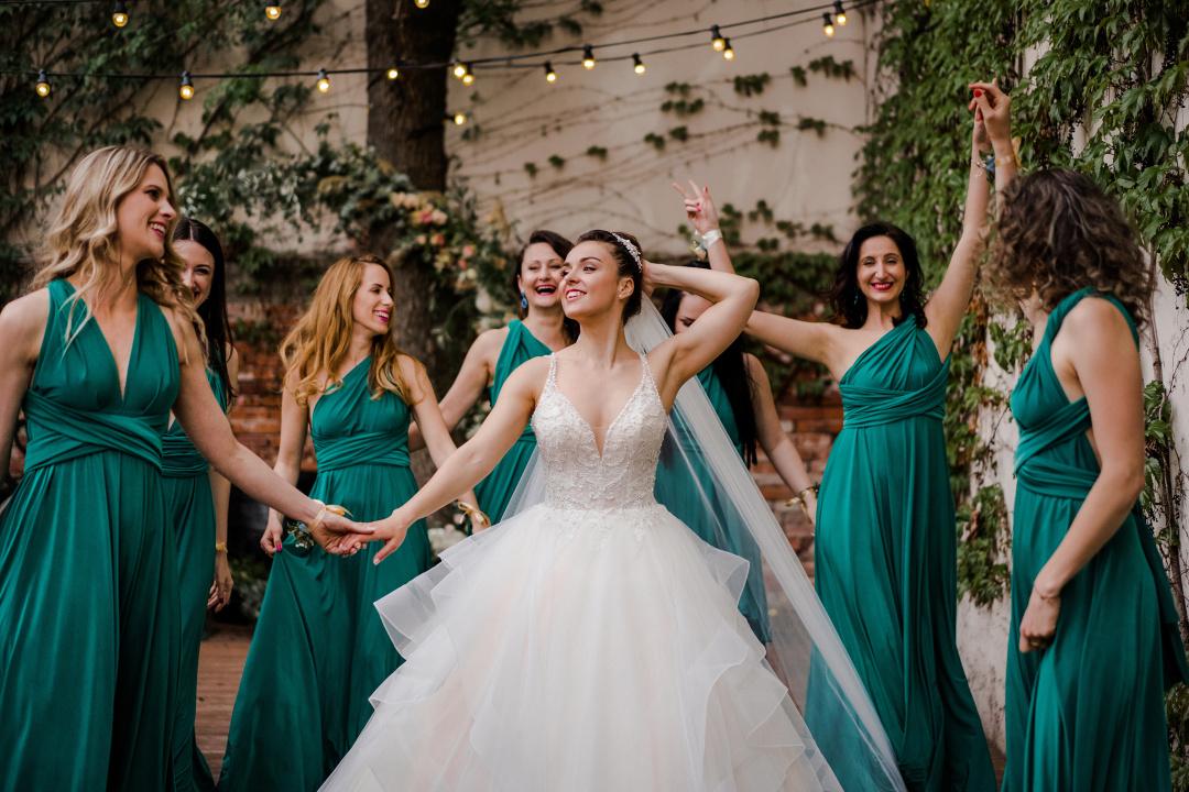 Družičky na svadbu v smaragdových šatách tancujú na parkete ozdobeným svetielkami. 